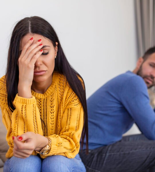 Sad pensive young girl thinking of relationships problems sitting on sofa with offended boyfriend, conflicts in marriage